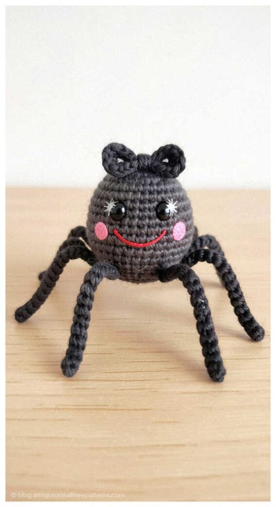 Gray amigurumi spider with pink cheeks standing on a wooden surface, free crochet spider pattern idea