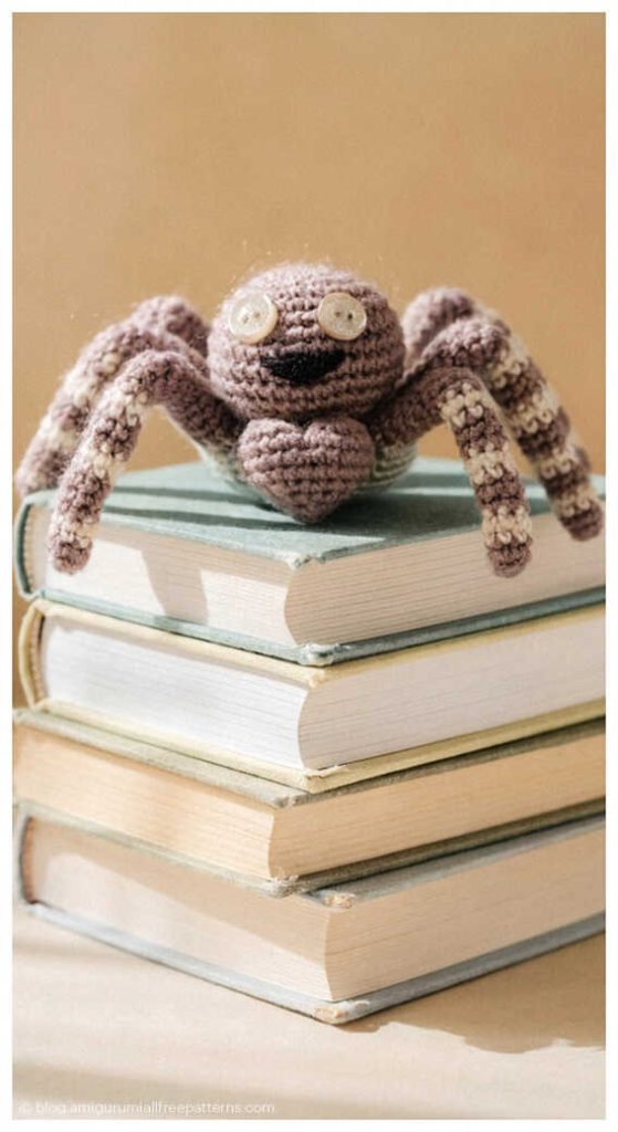 Brown amigurumi spider with long legs sitting on a stack of books, free crochet spider pattern inspiration