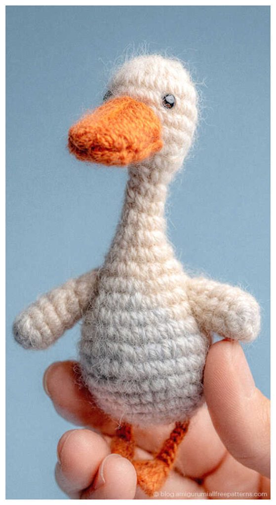 Cute amigurumi goose crochet toy with long neck held between fingers, handmade crochet goose plush