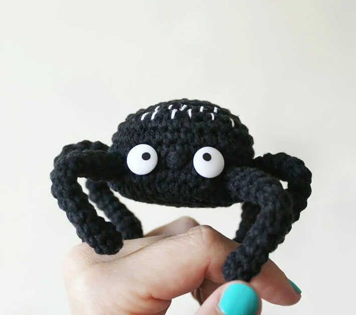 Black amigurumi spider with big round eyes held in hand, free crochet spider pattern for beginners
