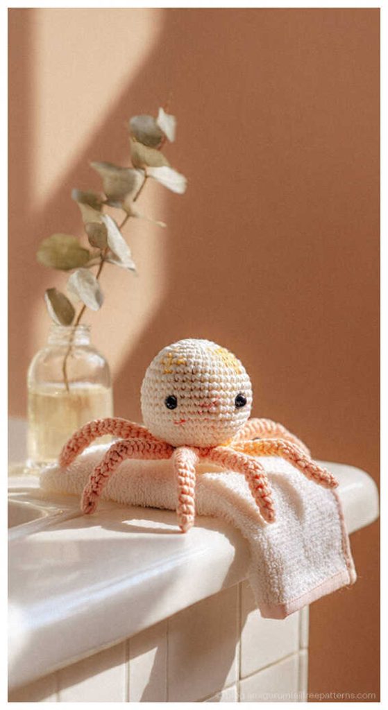 Small peach amigurumi spider sitting on a bathroom counter with a soft towel, free crochet spider pattern idea