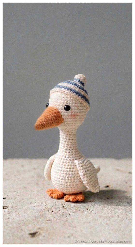 Small amigurumi goose crochet toy wearing a striped hat, adorable crochet goose plush