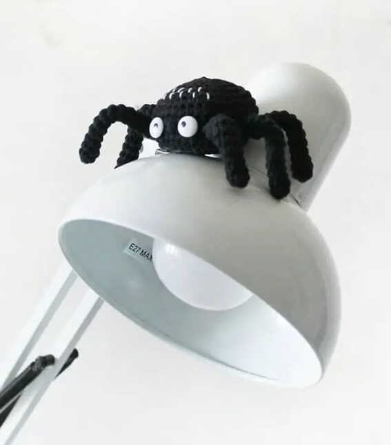Black amigurumi spider sitting on a white desk lamp, free crochet spider pattern for beginners