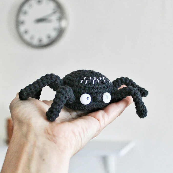 Handmade black crochet spider with large white eyes resting on a palm, free amigurumi spider pattern for beginners