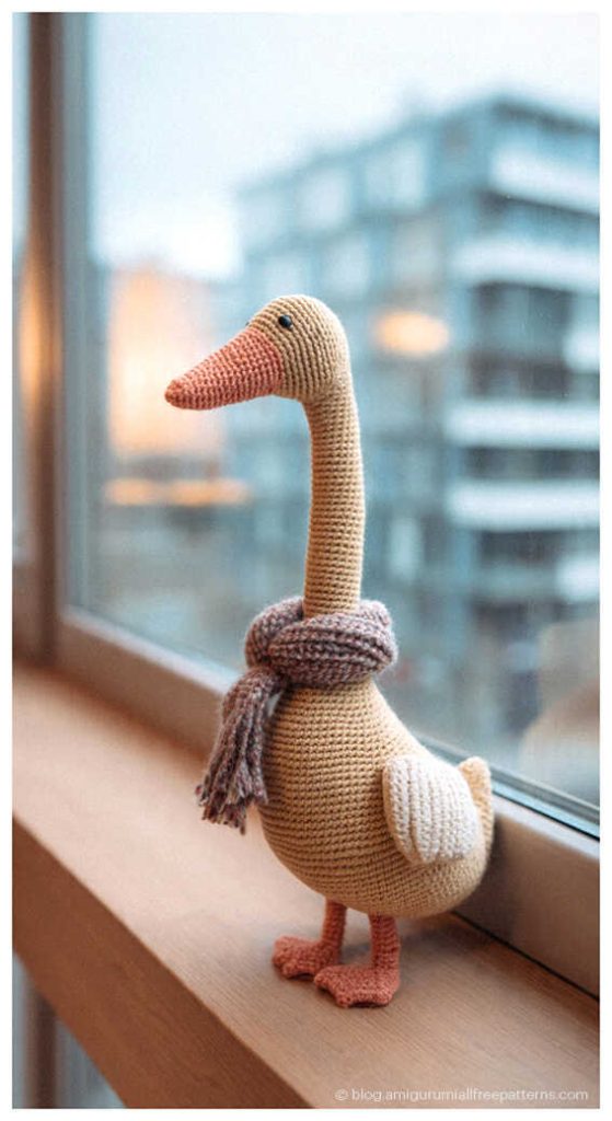 Cute amigurumi goose crochet toy wearing a scarf by the window, handmade crochet goose plush