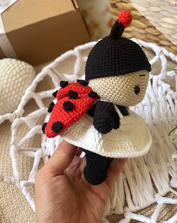 Amigurumi ladybug doll side view with red wings and black spots held in hand, free crochet ladybug pattern