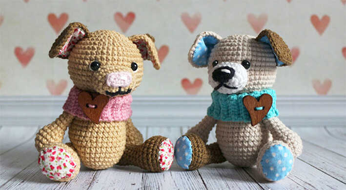 Two amigurumi puppy dogs with scarves and heart details sitting on wooden floor, free crochet dog pattern