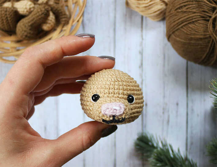 Amigurumi puppy head held between fingers with yarn background, free crochet dog pattern