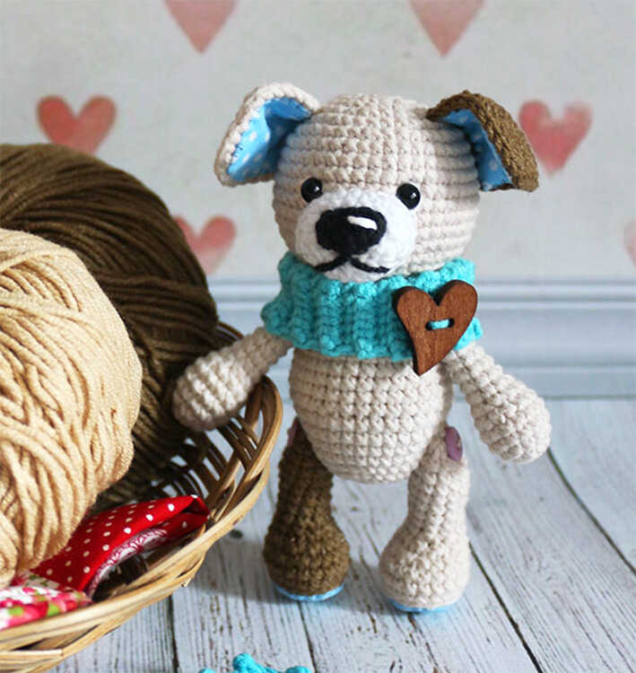 Amigurumi puppy dog with blue scarf and heart detail standing next to yarn basket, free crochet dog pattern
