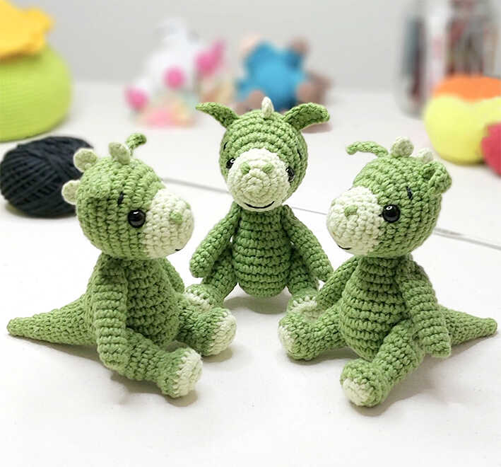 Three cute green amigurumi dragons sitting on a table, free crochet dragon pattern for beginners