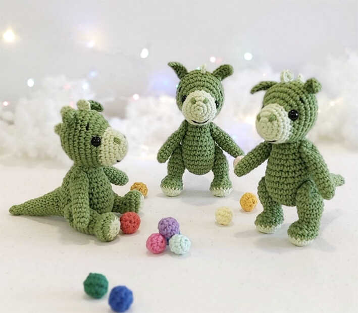 Three small green amigurumi dragons standing together with colorful yarn balls, free crochet dragon pattern