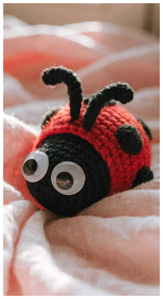 Amigurumi ladybug crochet toy lying on soft fabric, cute crochet ladybug plush