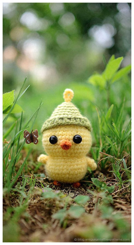 Amigurumi chick crochet toy wearing a small hat outdoors in grass, adorable crochet chick toy