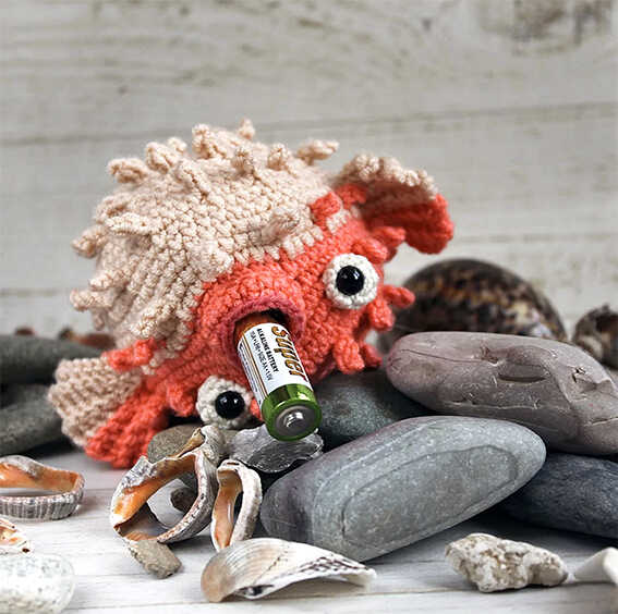 Spiky amigurumi puffer fish crochet toy resting on beach stones with seashells, free crochet fish pattern