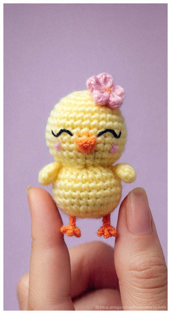 Tiny amigurumi chick crochet toy with a pink flower held between fingers, adorable crochet chick gift