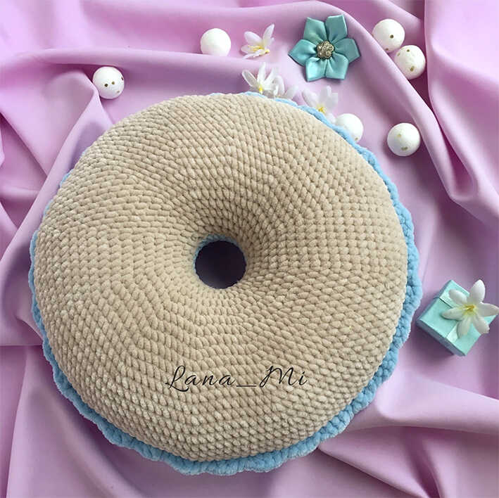 Back side of amigurumi donut pillow in beige with blue edge on fabric background, free crochet donut cushion pattern